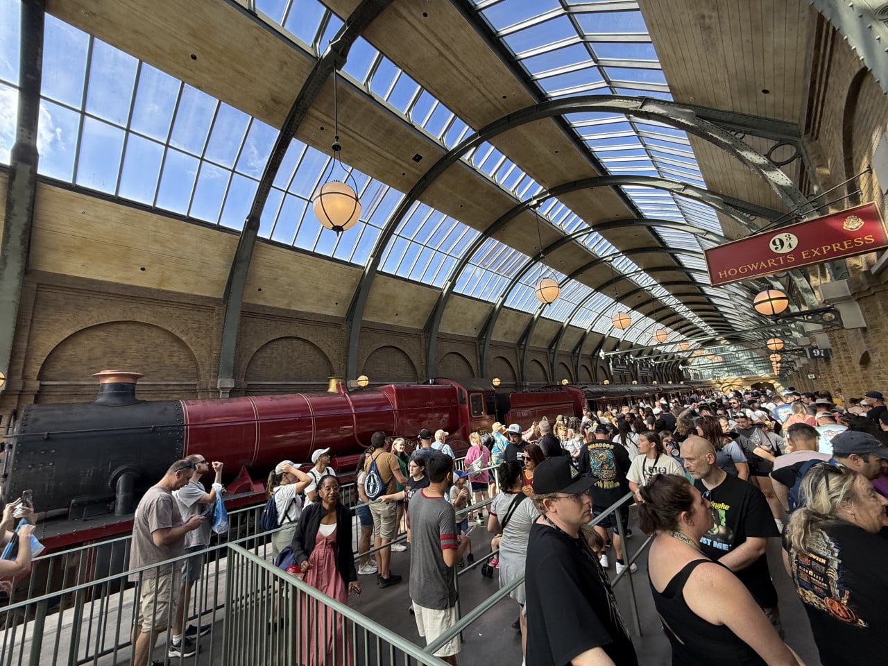 Fronta lidí u vlaku Hogwarts Express na nádraží s prosklenou střechou.