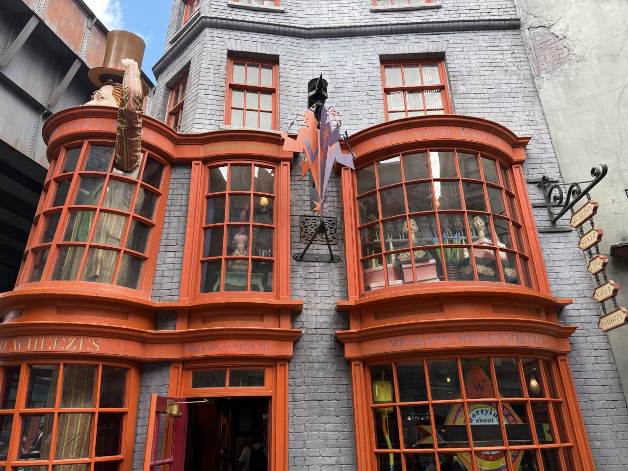 Fasáda obchodu Weasleys’ Wizard Wheezes s oranžovými okny a figurínou kouzelníka nahoře