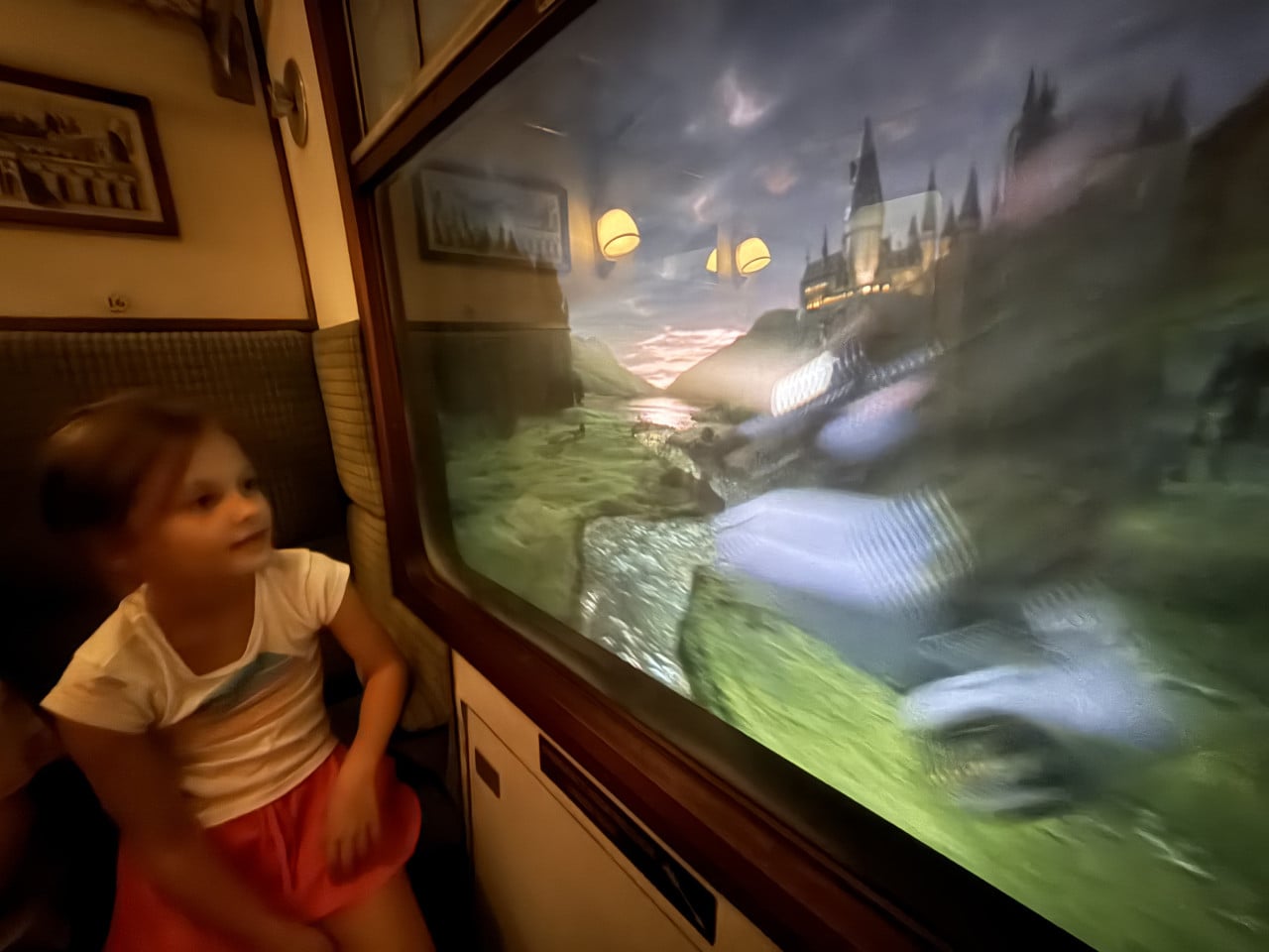 Dívka sedí ve vagónu a dívá se na projekci hradu u jezera v Universal Studios Orlando
