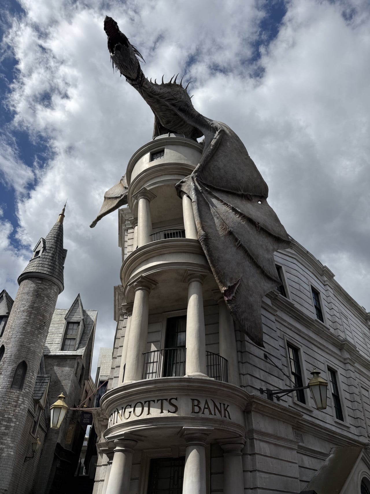 Drak sedící na budově Gringotts Bank v kouzelnické ulici pod oblačnou oblohou