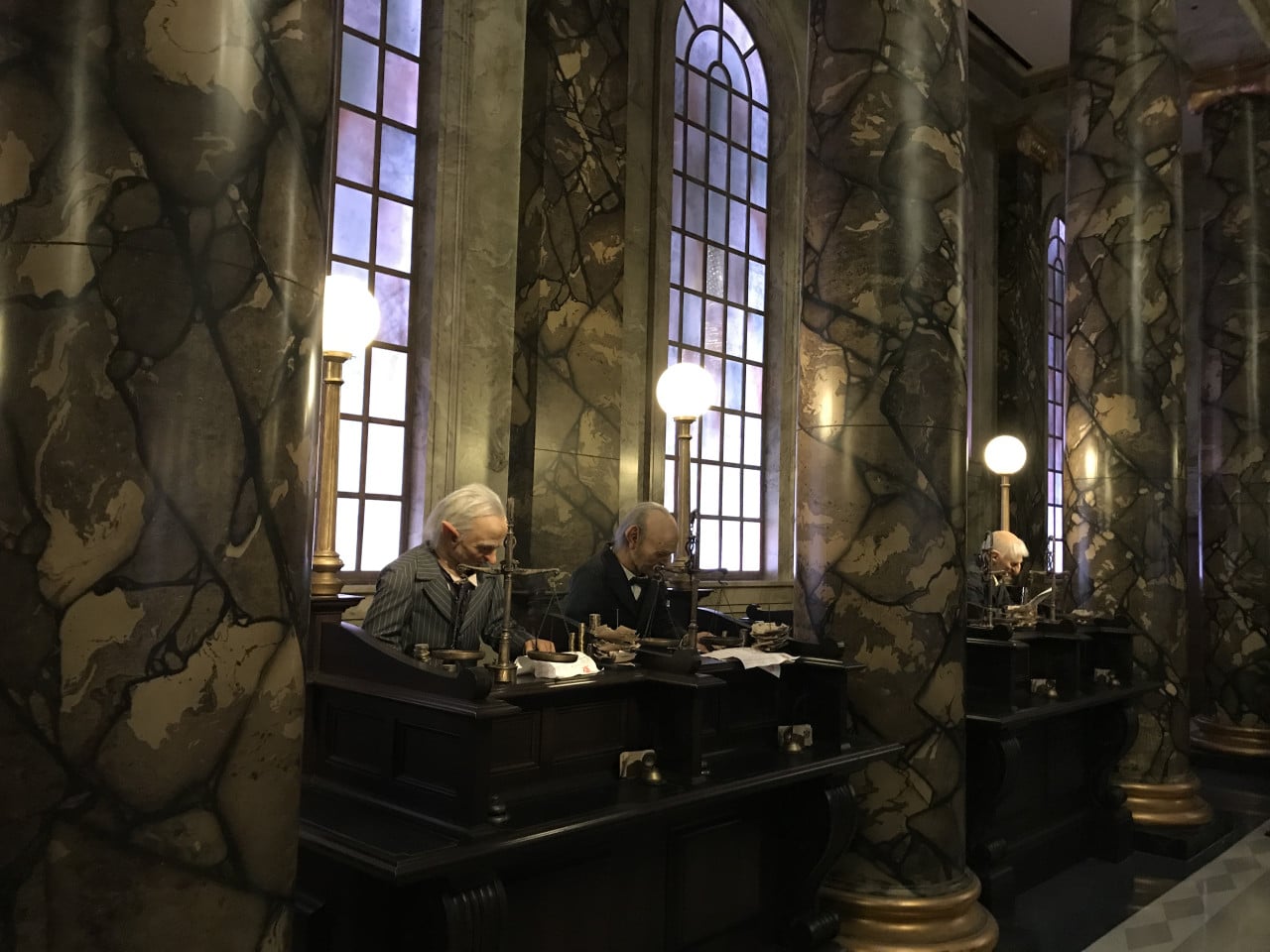 Elfi u přepážek v kouzelné bance Gringott s mramorovými sloupy a lampami