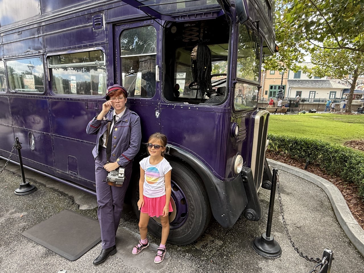 Dívka a průvodkyně stojí u fialového kouzelnického autobusu Universal Studios Orlando.