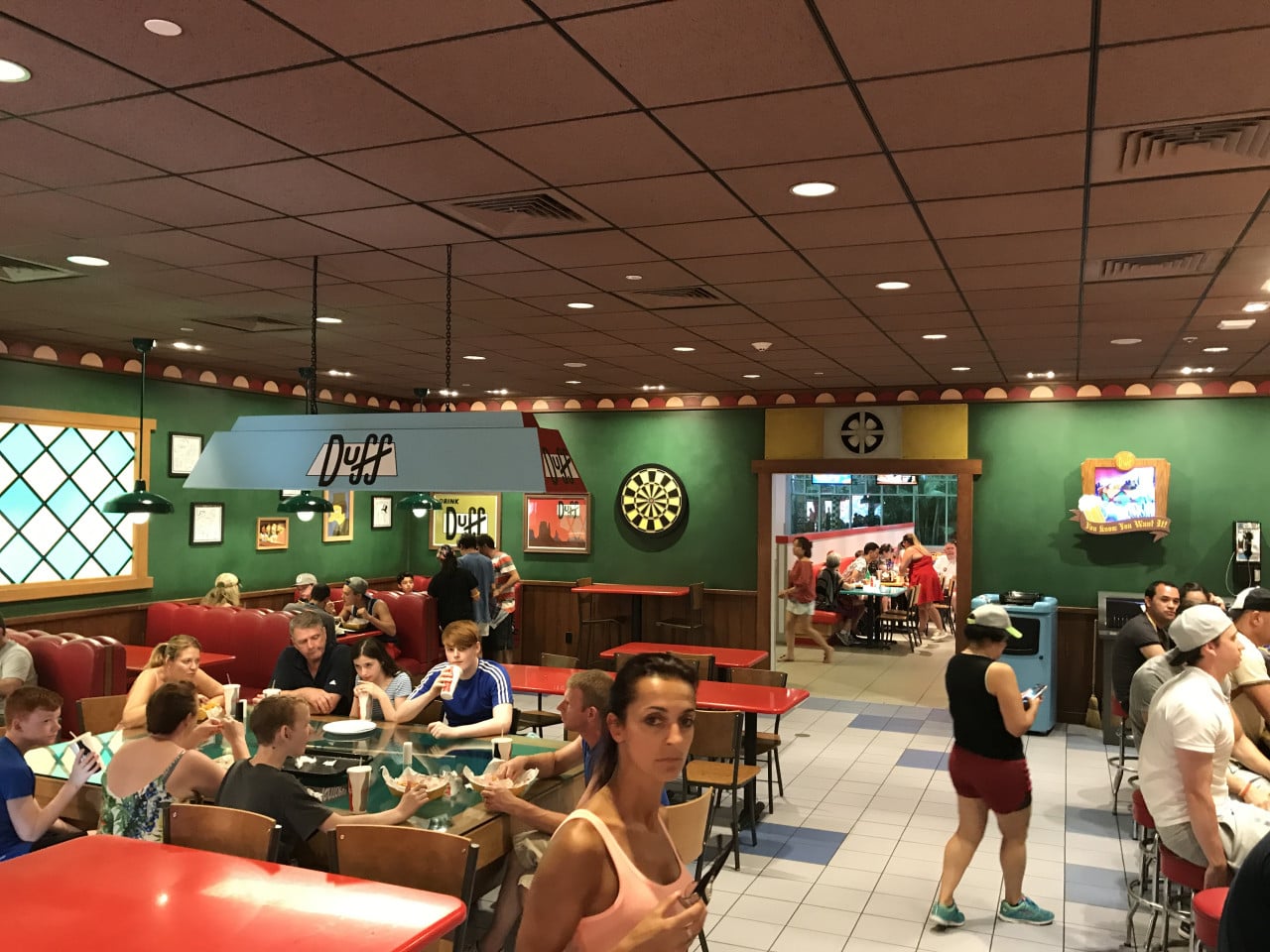 Rodinná restaurace Duff s návštěvníky, stoly a dartboardem v Universal Studios Orlando