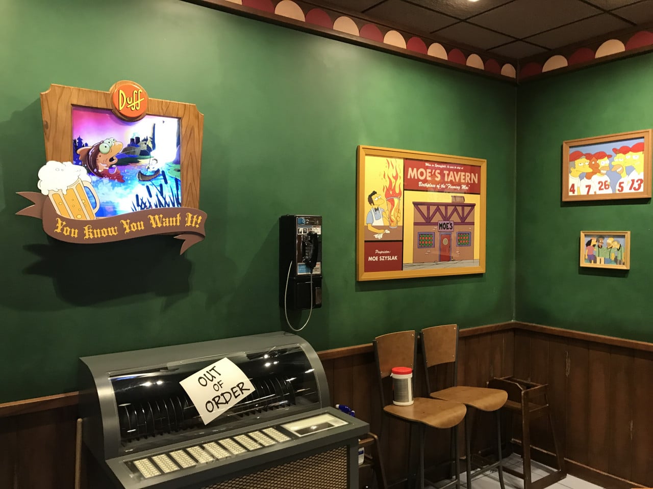 Interiér Simpsonovského baru s cedulemi Duff a Moe’s Tavern, telefonem a automatem out of order