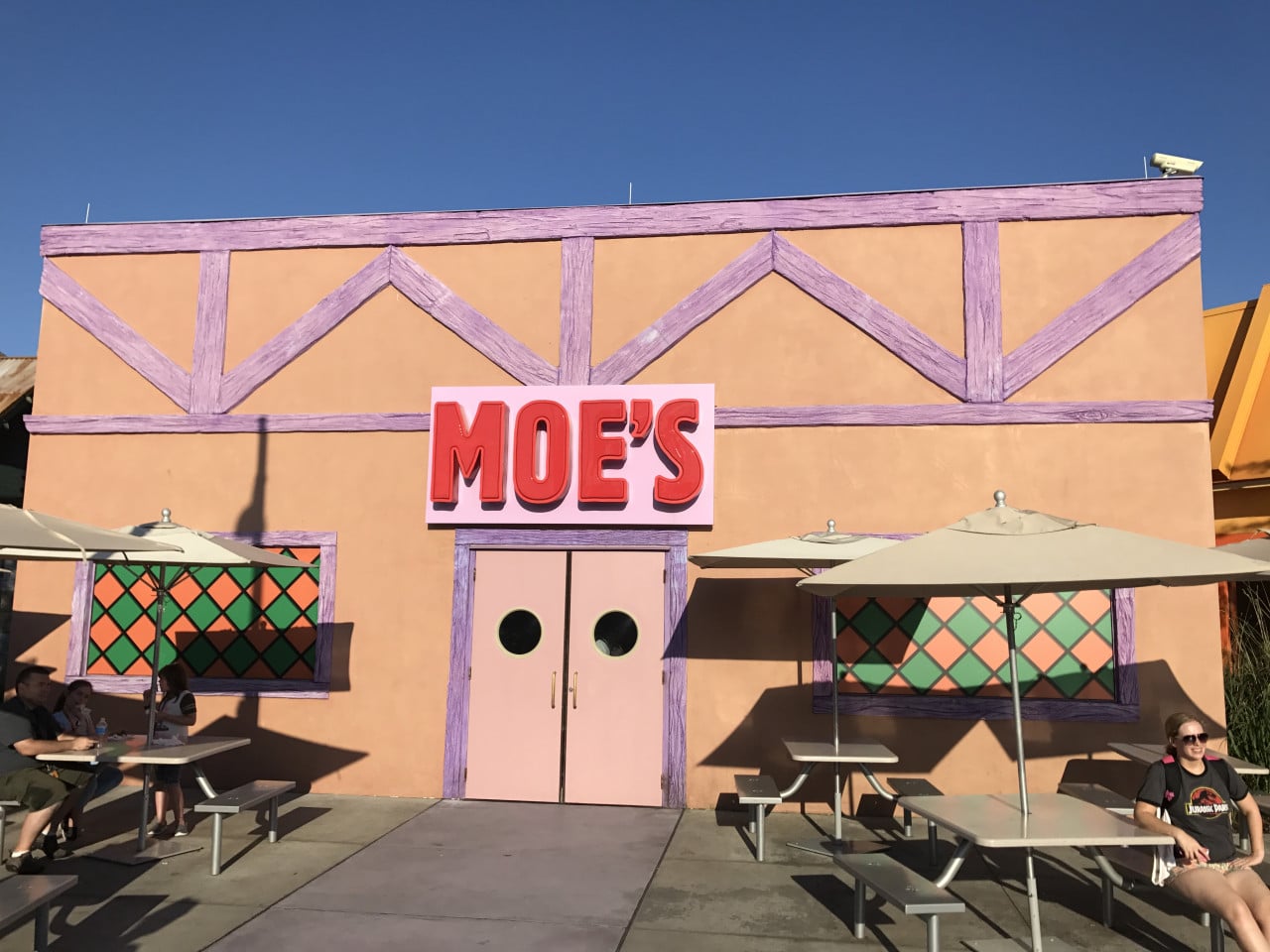 Fasáda restaurace Moe’s s růžovými dveřmi a venkovním posezením na slunci