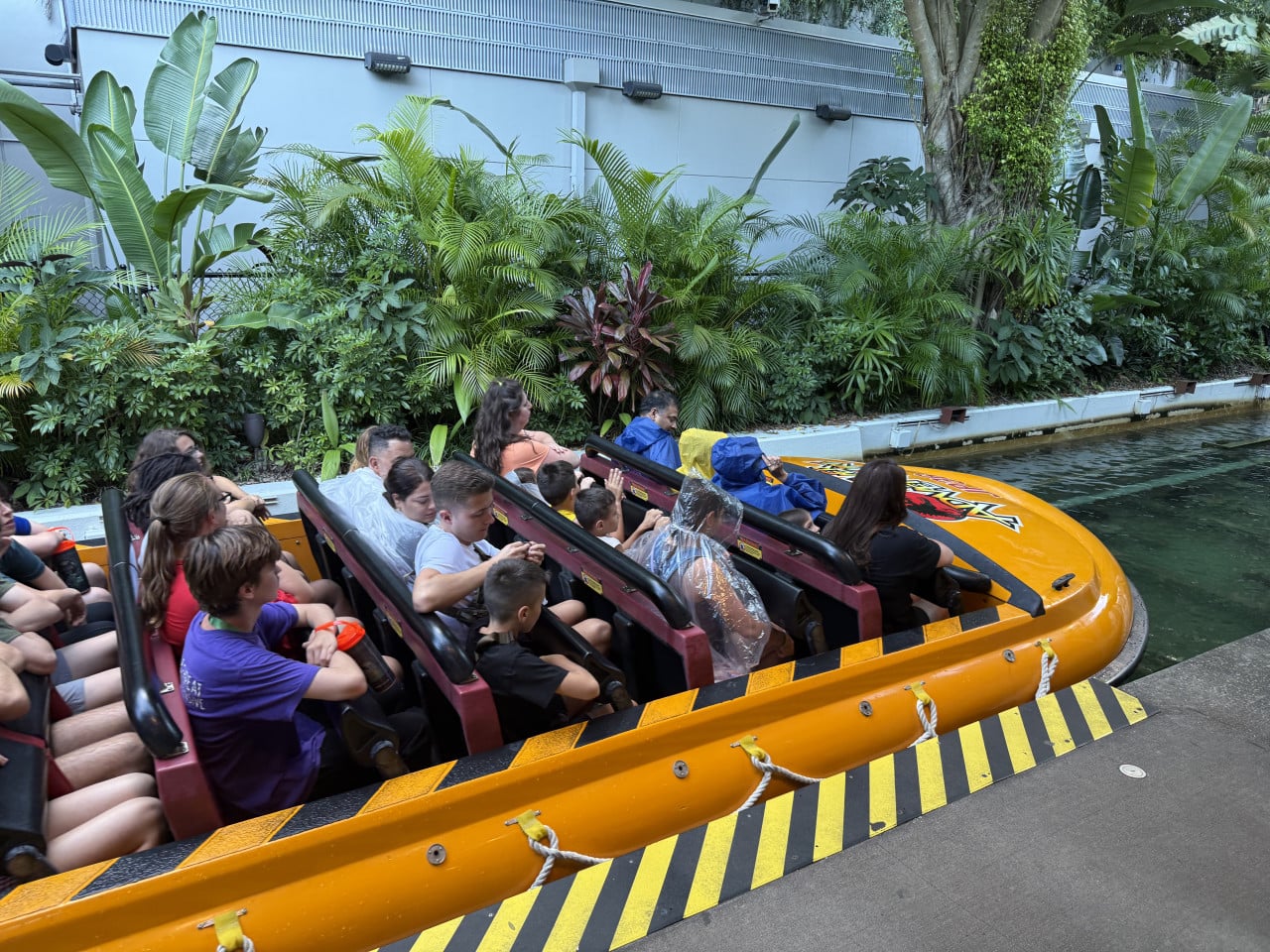 Lidé sedí v oranžové raftové lodi na atrakci mezi tropickými rostlinami v Universal Studios Orlando