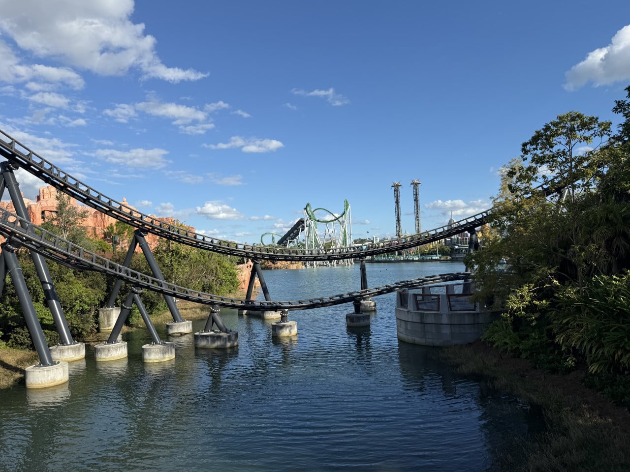 Dráha horské atrakce nad vodou v Universal Studios Orlando, modrá obloha a zelené kopce.