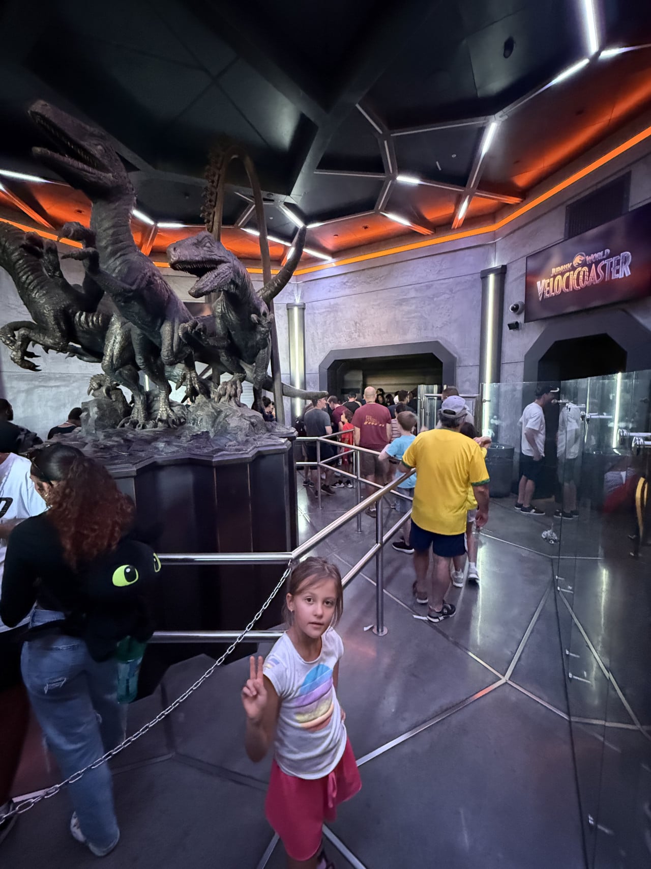 Fronta na atrakci Velocicoaster v Universal Studios Orlando, dítě v popředí ukazuje mír znakem vítězství.