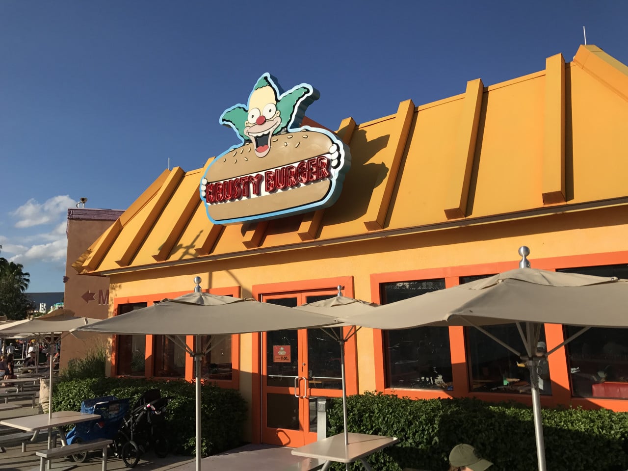 Restaurace Krusty Burger s barevnou cedulí a slunečníky před vstupem v Universal Studios Orlando