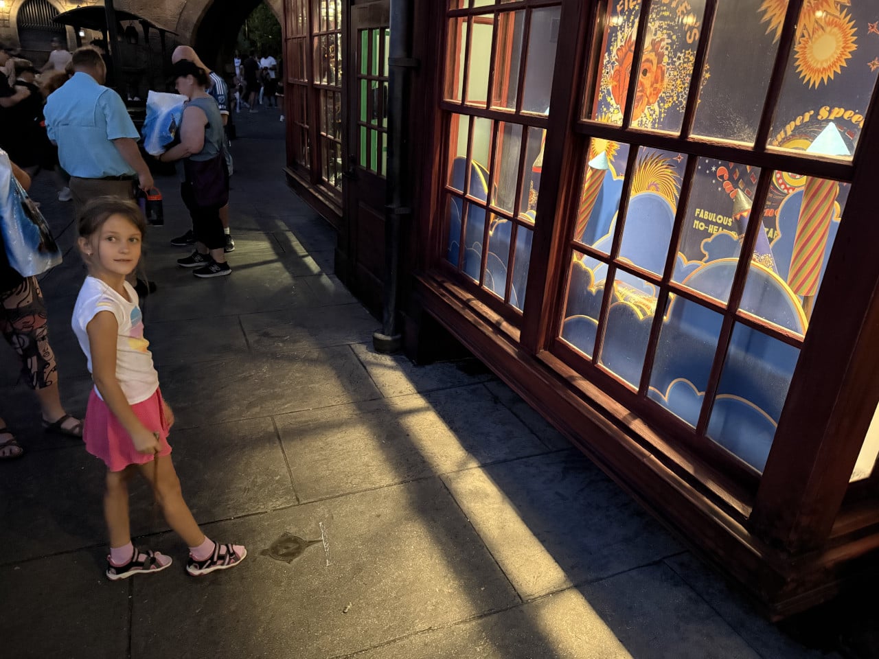 Dívka v parku Universal Studios stojí u výlohy s barevnými retro motivy a textem.