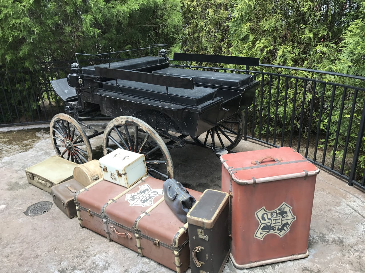 Černý kočár s kufry a zavazadly před zeleným plotem v Universal Studios Orlando