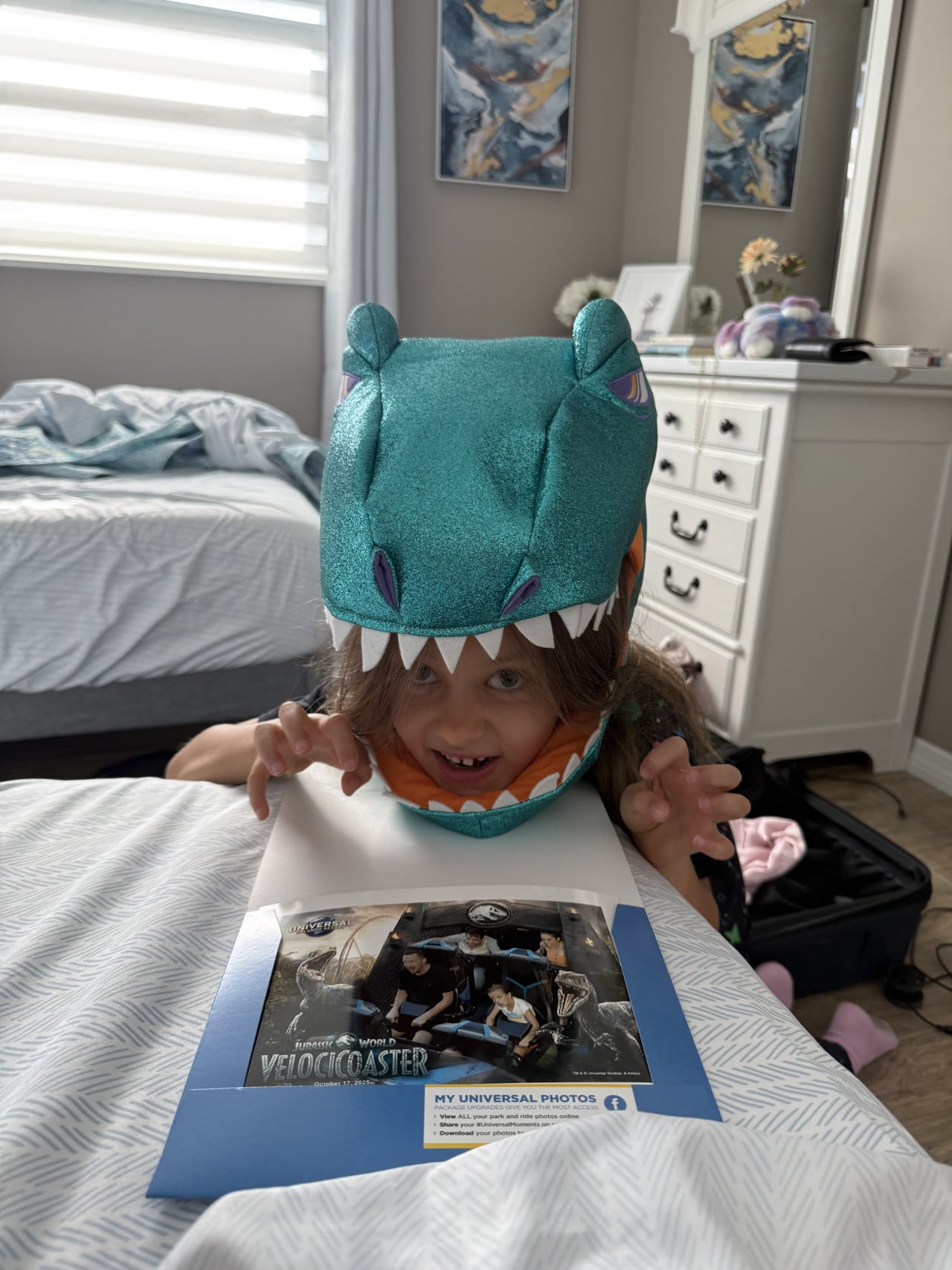 Dítě v dinosauří helmě drží fotografii z Jurassic World VelociCoaster v ložnici.