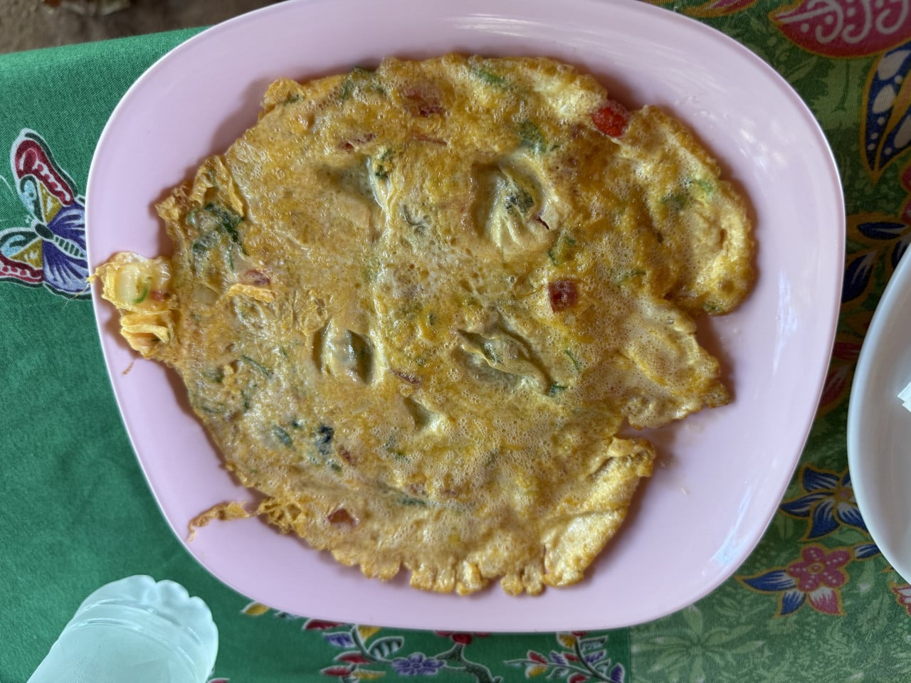 Omeleta s bylinkami a kousky zeleniny na růžovém talíři na vzorovaném ubrusu