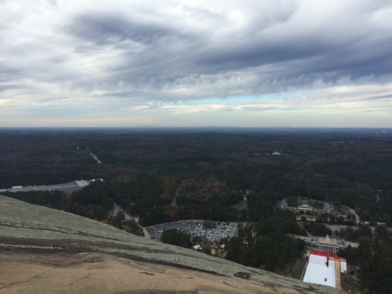 Výhled ze skály Stone Mountain na lesy, parkoviště a budovy pod zataženou oblohou.