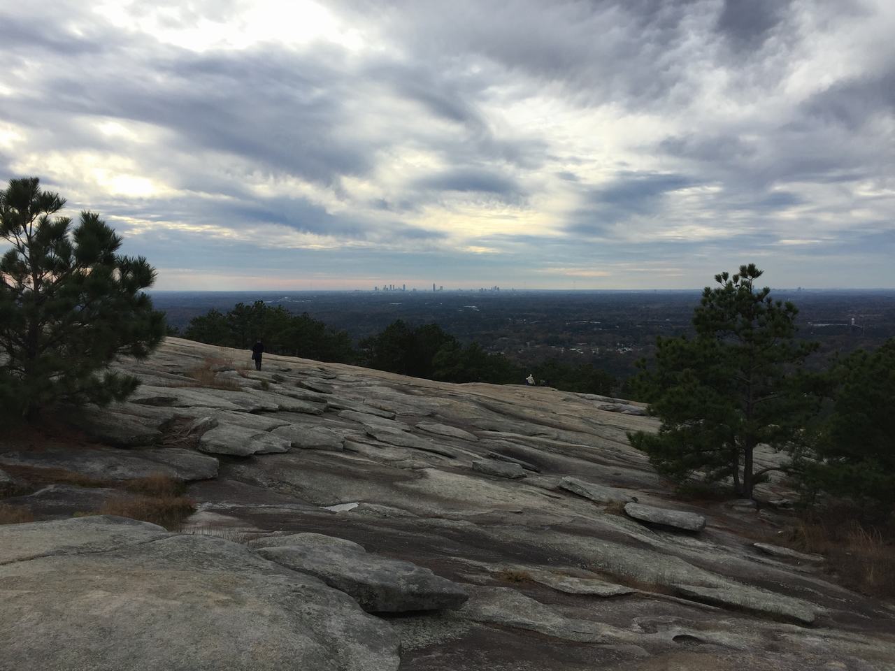 Žulová plošina Stone Mountain s turisty, stromy a vzdáleným panoramatem Atlanty pod mraky