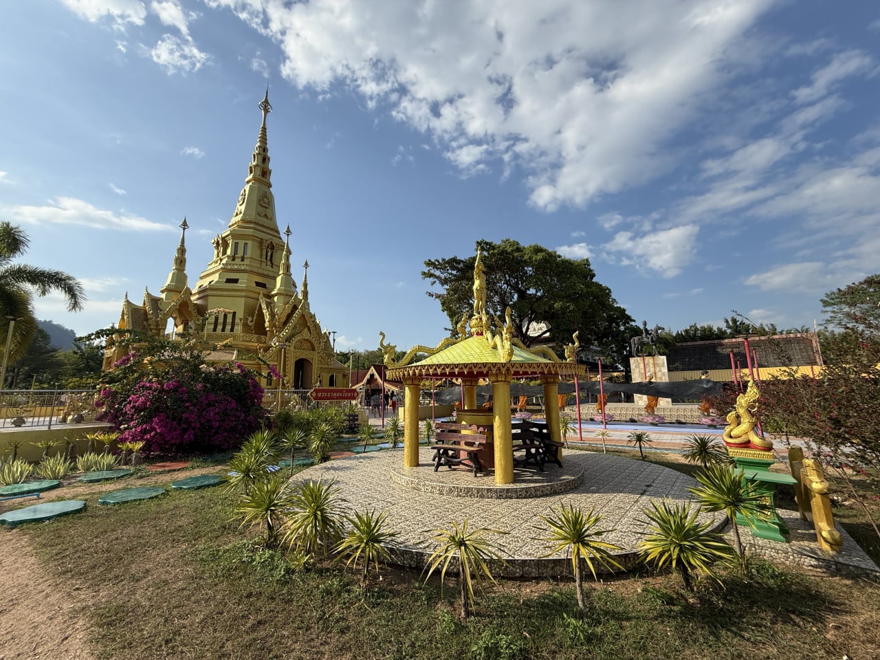 Zlatý buddhistický chrám se stúpou, pavilon s lavičkami a zahrada pod modrou oblohou