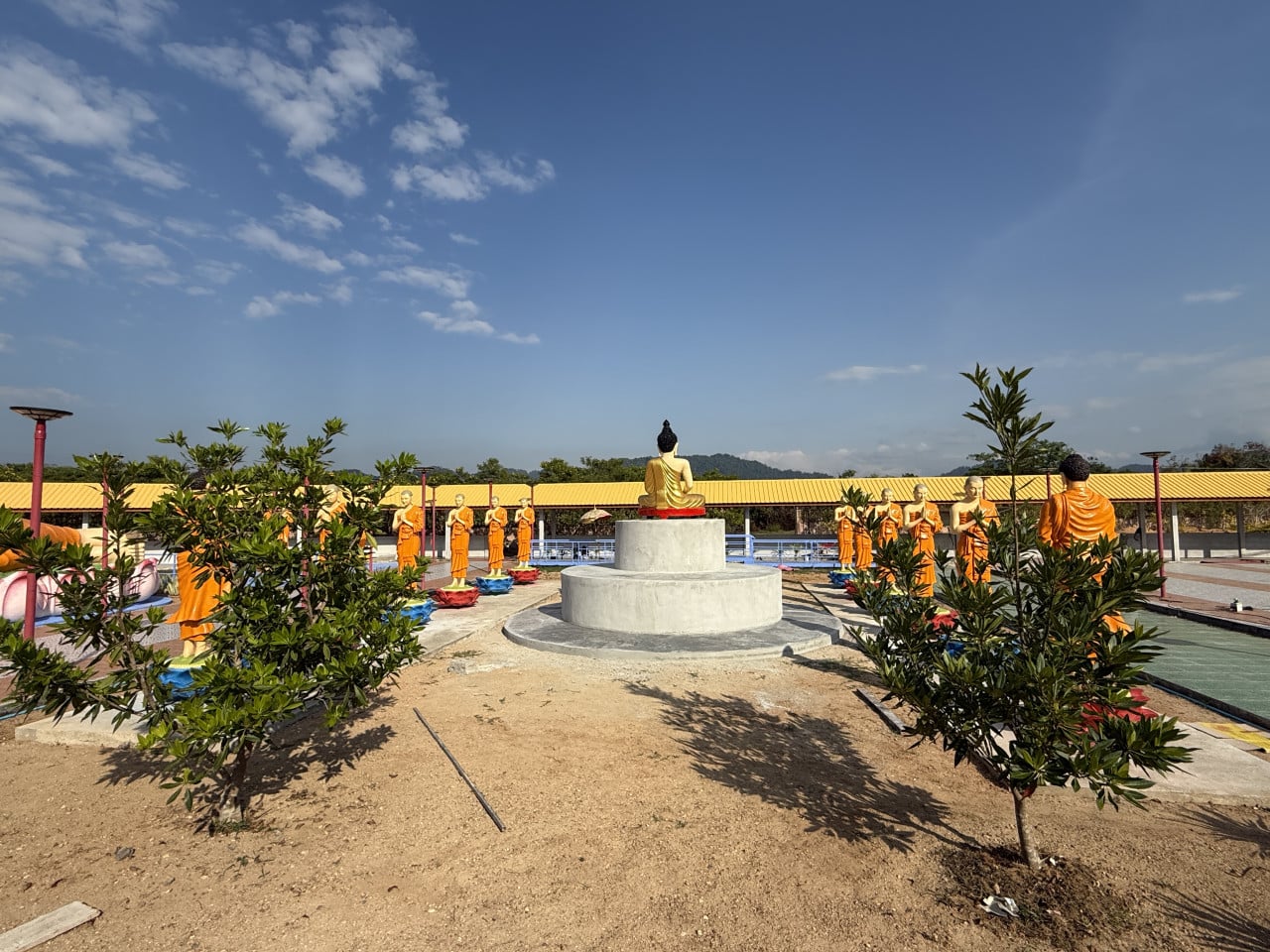 Socha sedícího Buddhy na podstavci, kolem stojící mniši v oranžových róbách.