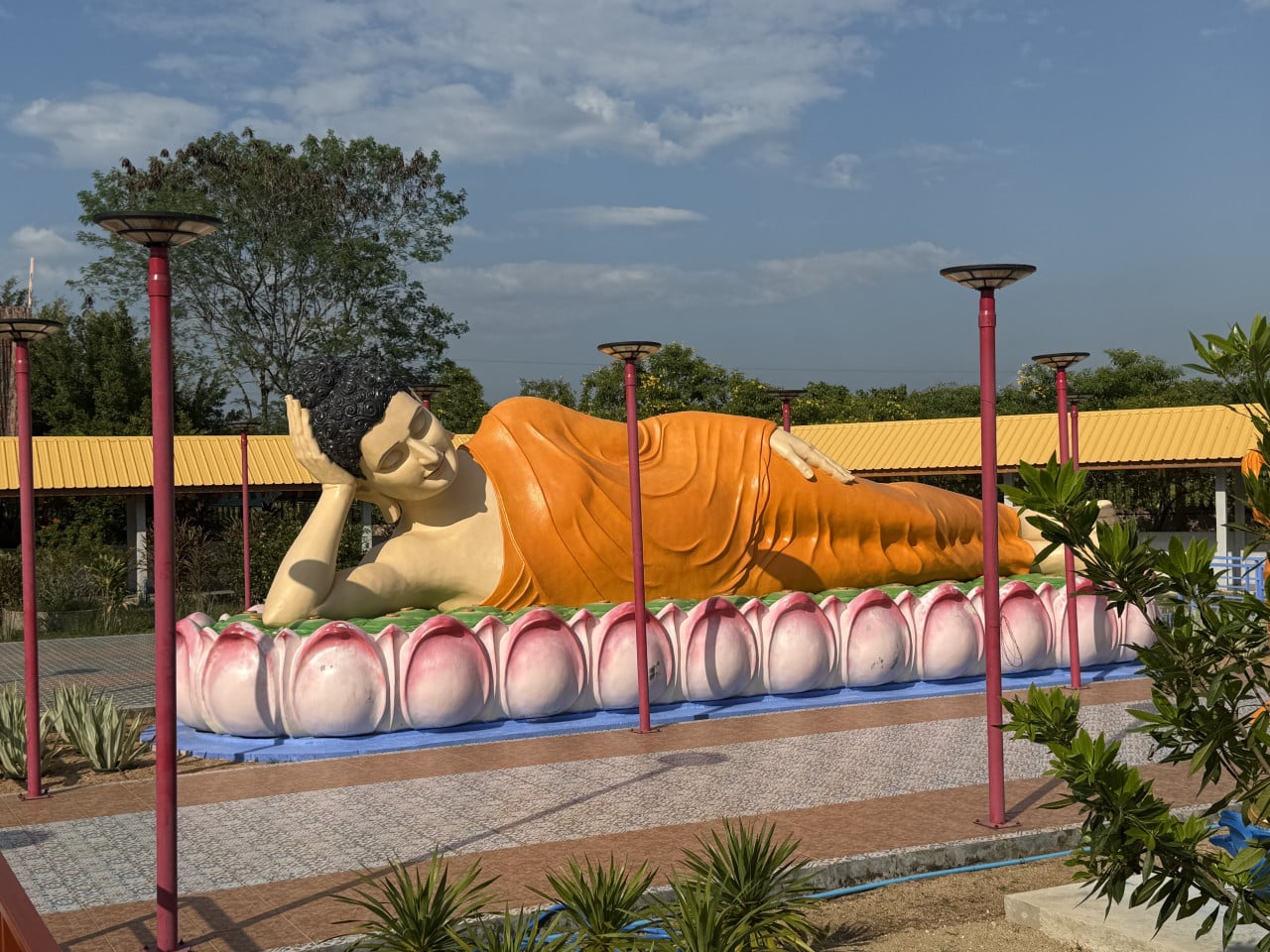 Ležící socha Buddhy v oranžovém rouchu na růžovém lotosu, venku.