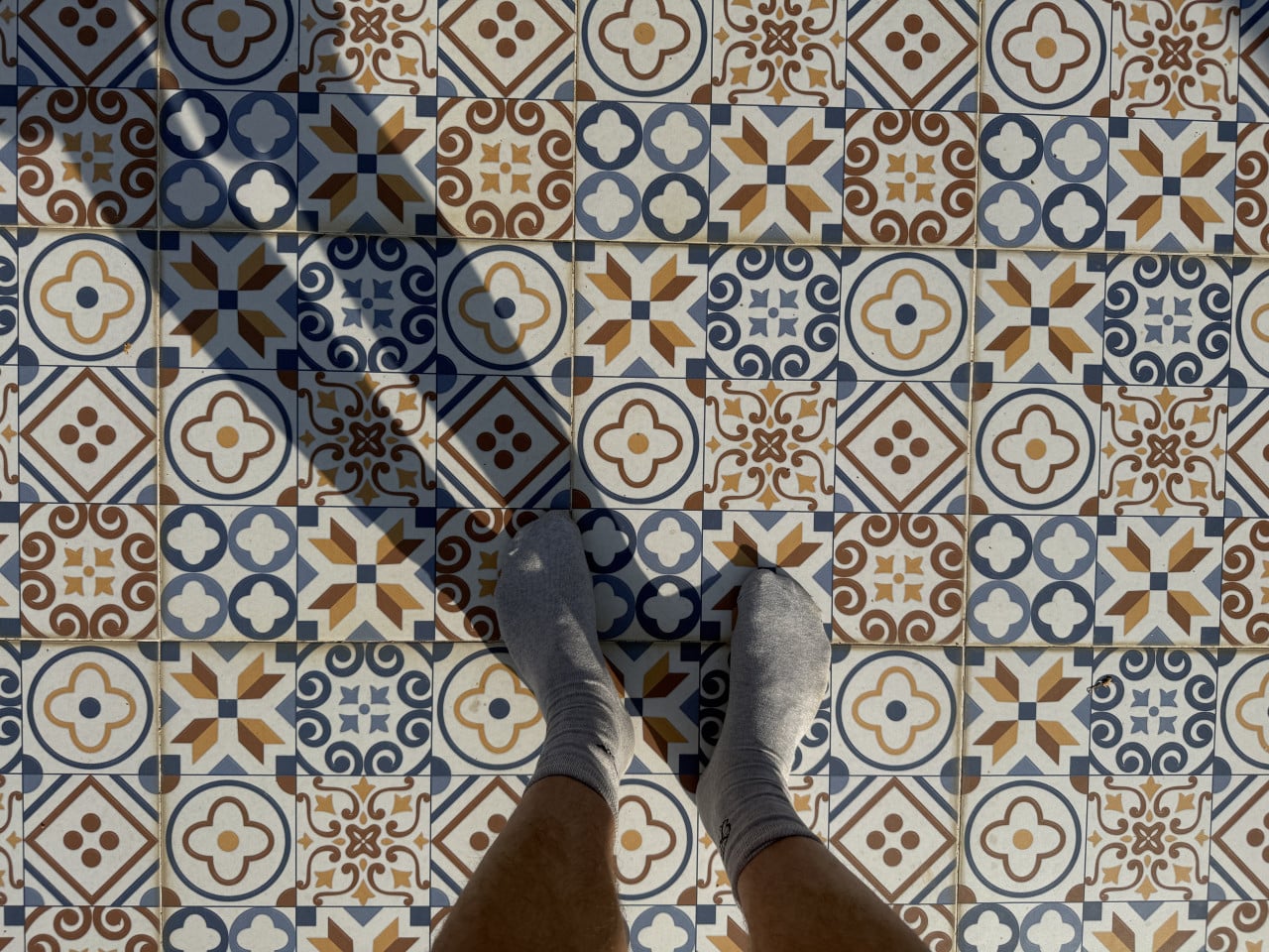 Nohy v šedých ponožkách na barevné vzorované dlažbě, záběr zblízka.