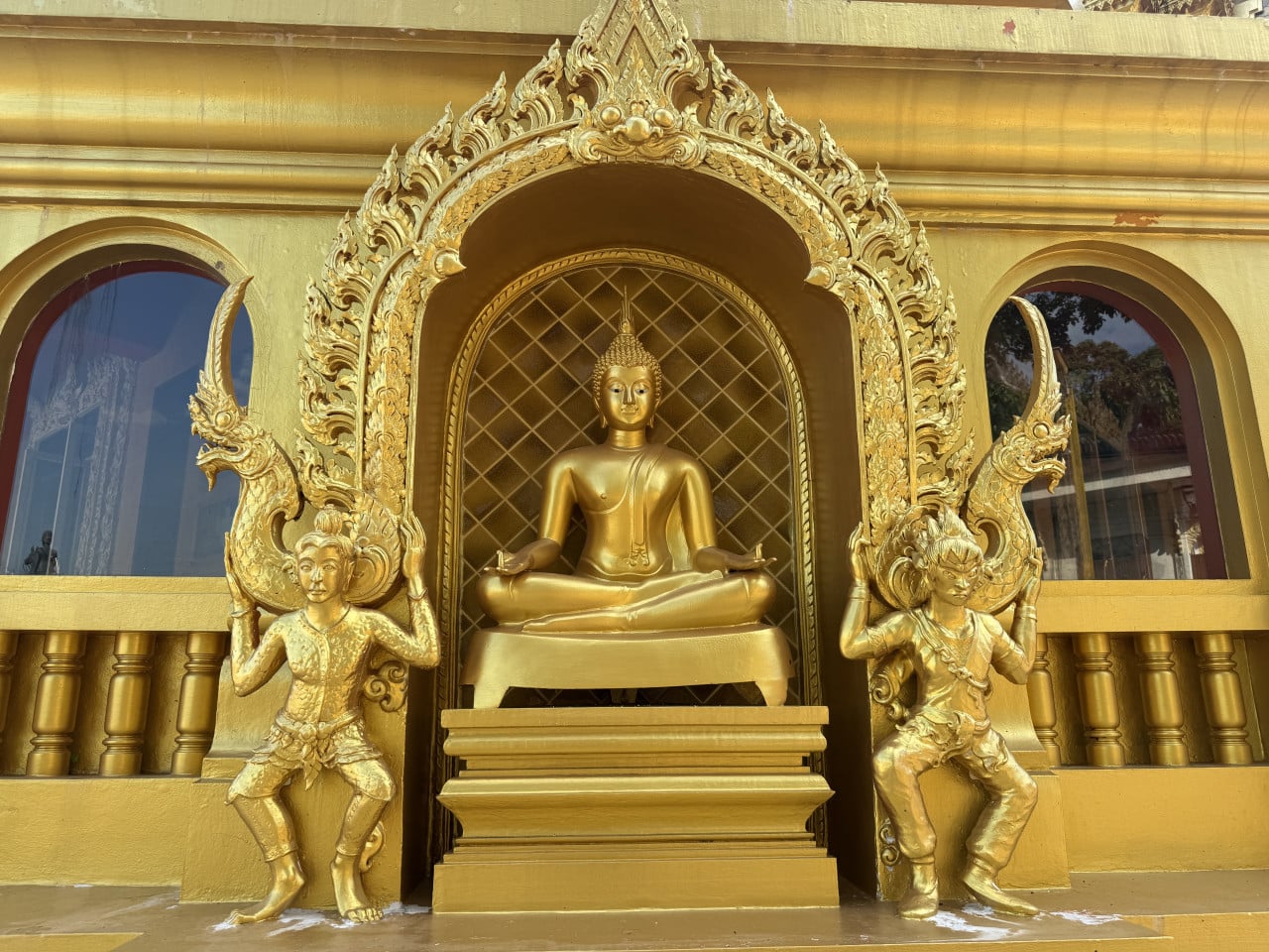 Zlatá socha sedícího Buddhy v nikách, po stranách dvě zlaté strážní postavy