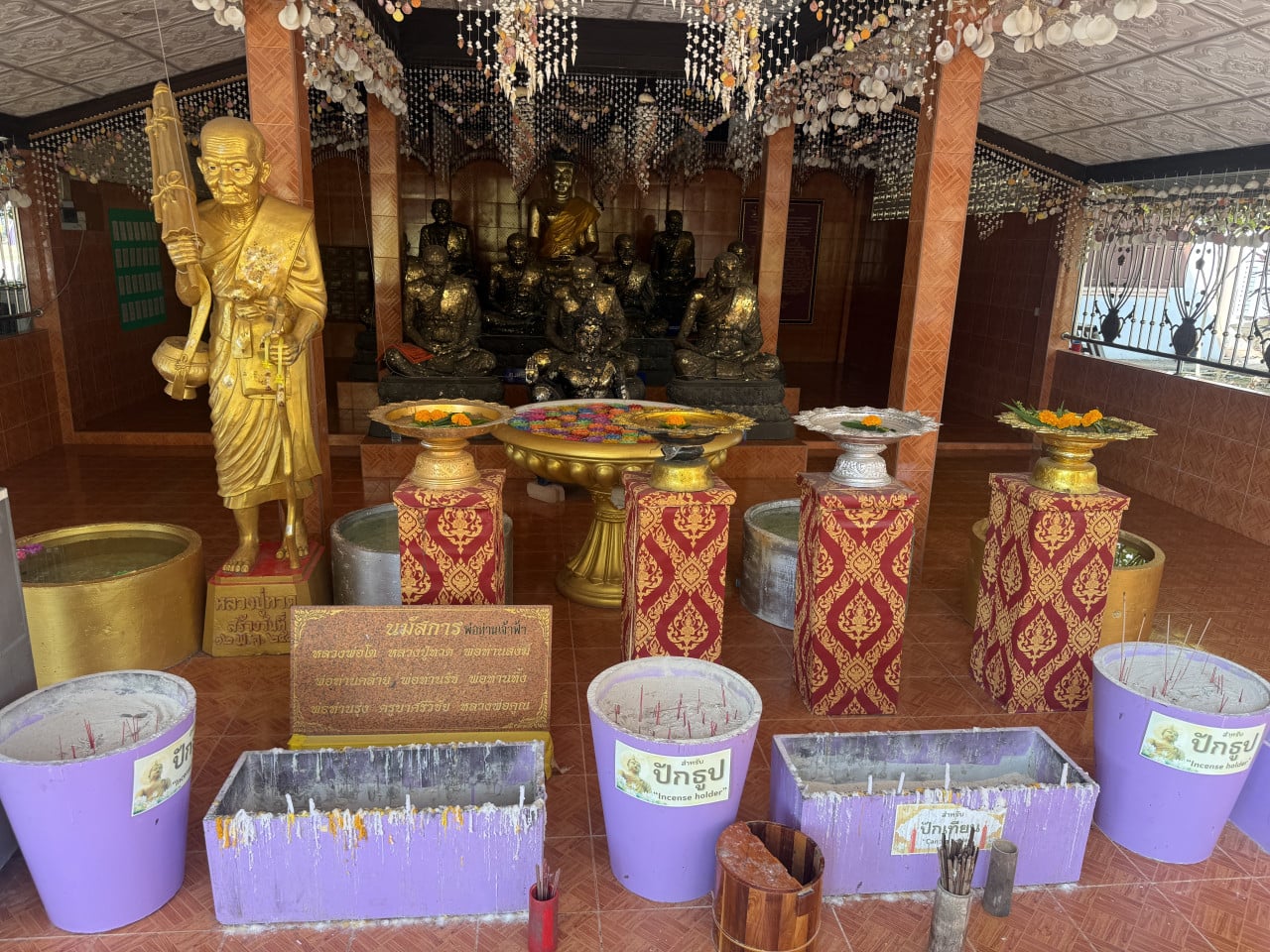 Zlatá socha mnicha, oltář s černými sochami, nádoby s nápisem incense holder.