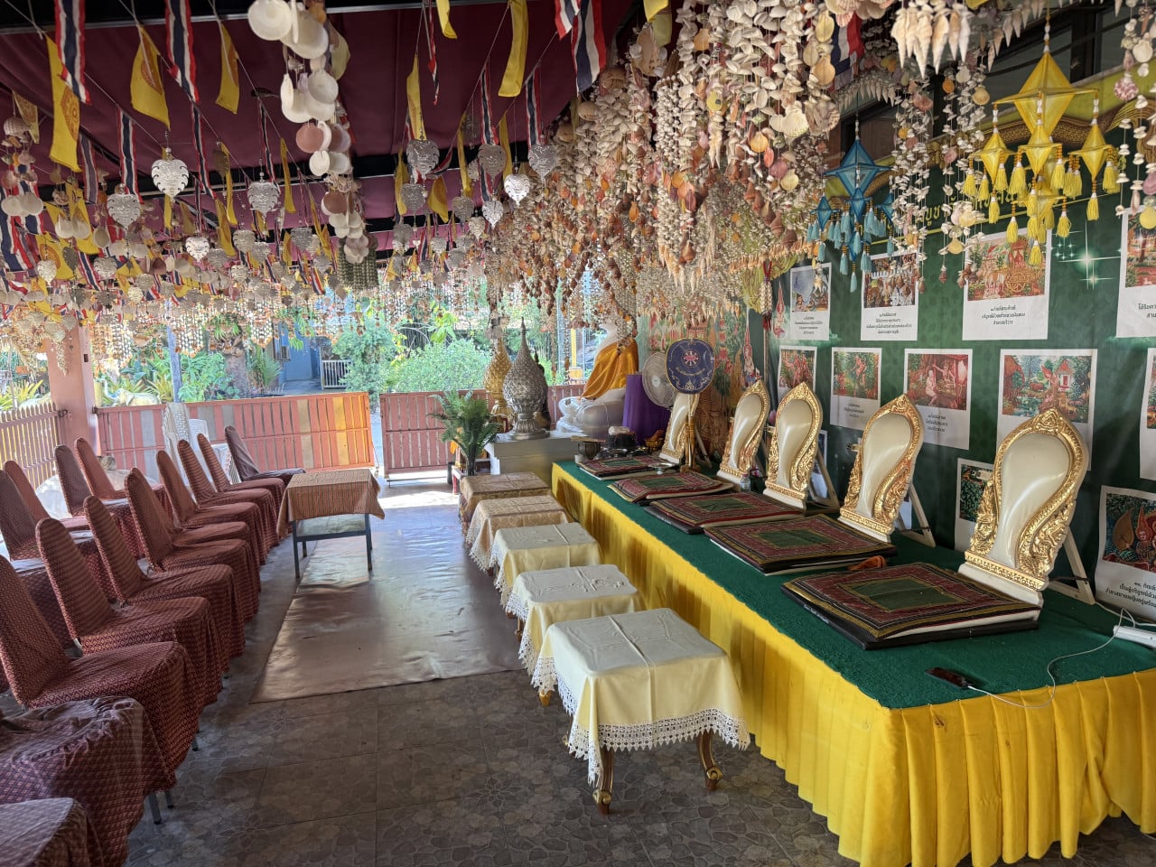 Interiér chrámu s řadou židlí, zdobeným oltářem a plakáty s thajským textem.