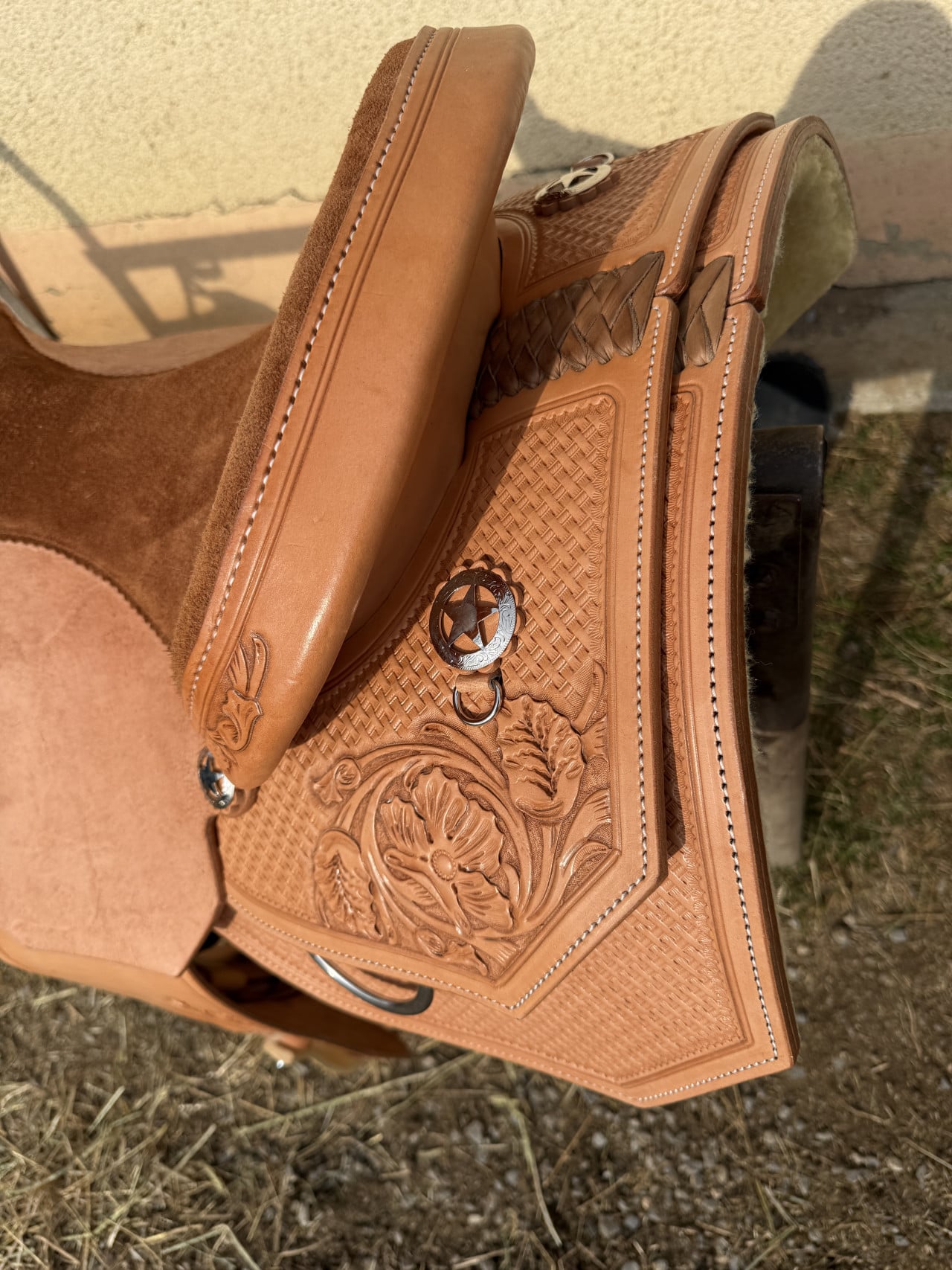 Detail koženého westernového sedla s vyřezávaným zdobením položeného na stojanu u stáje.