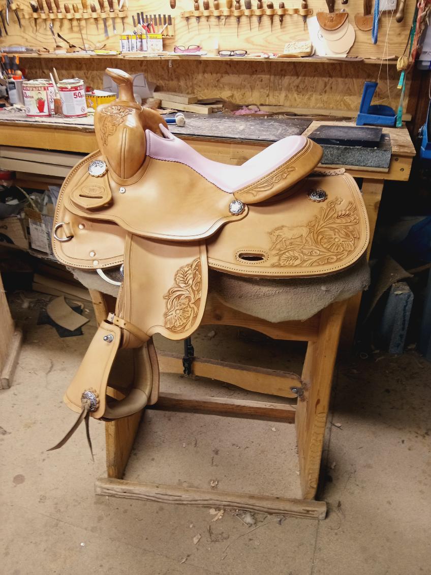 Ručně zdobené kožené westernové sedlo na stojanu v sedlářské dílně, nářadí vzadu.