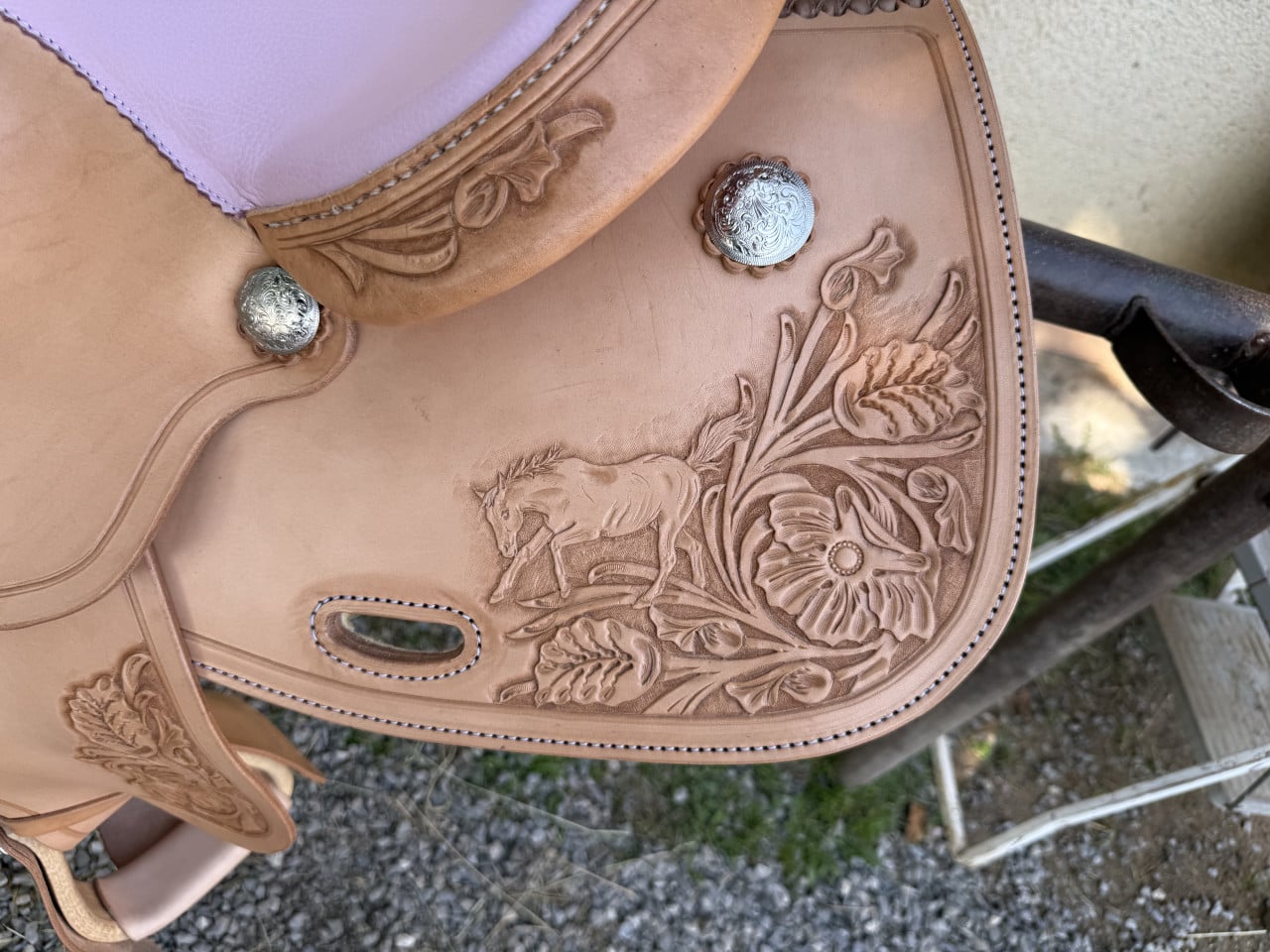 Detail ručně zdobeného westernového sedla: kožené rytiny květů, koně a stříbrné ozdoby
