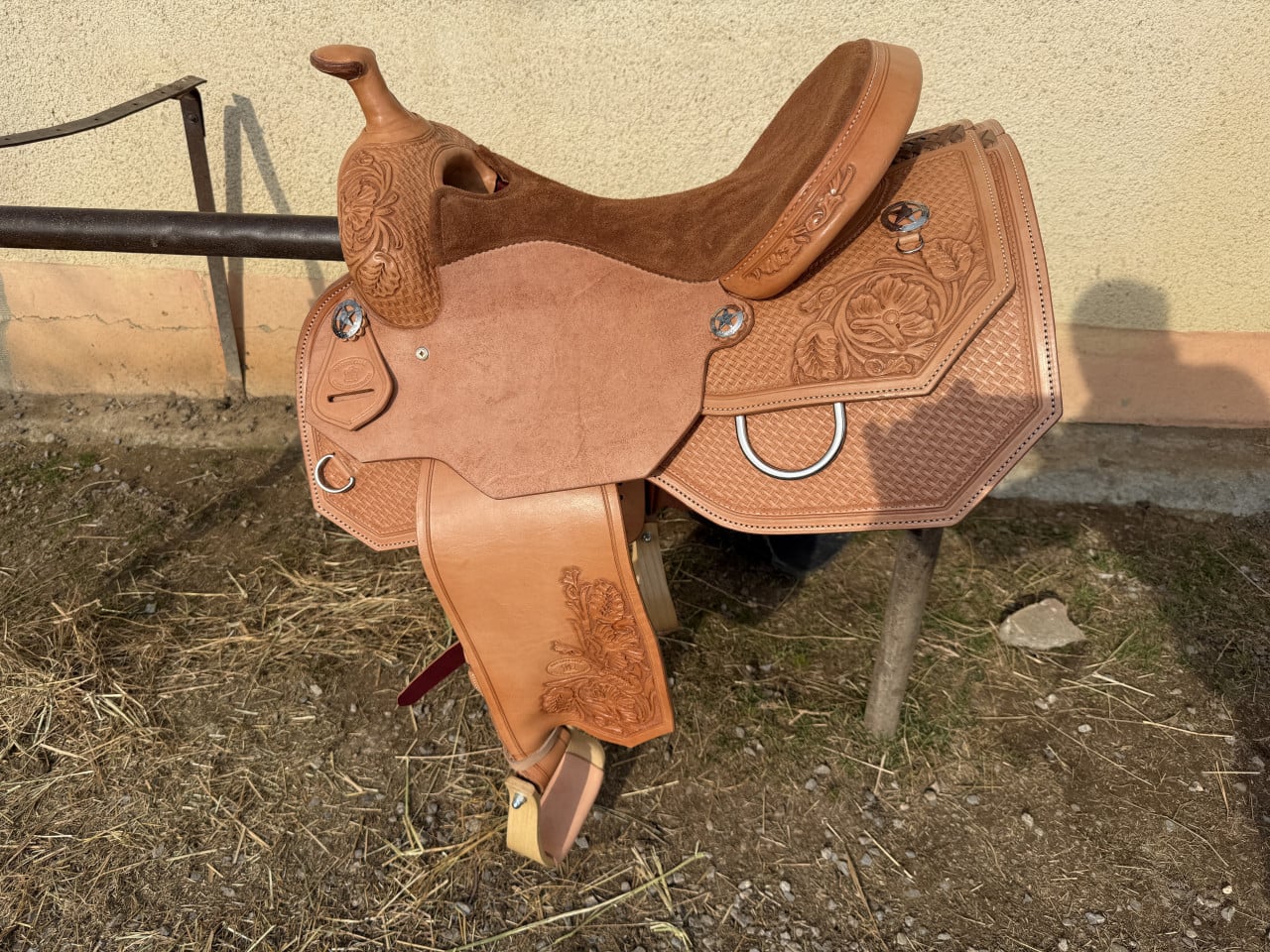 Hnědé westernové sedlo s vyřezávaným květinovým zdobením na stojanu u zdi.