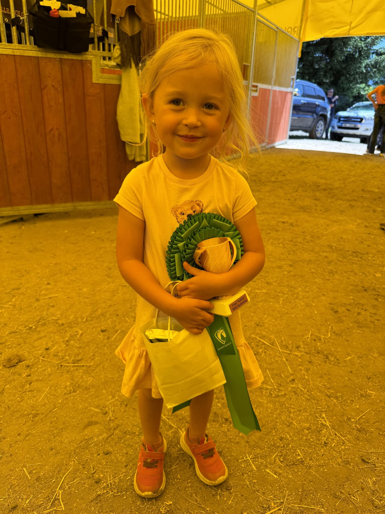 Malá dívka v hale drží zeleno-bílou stuhu a trofej s nápisem SMART RANCH.