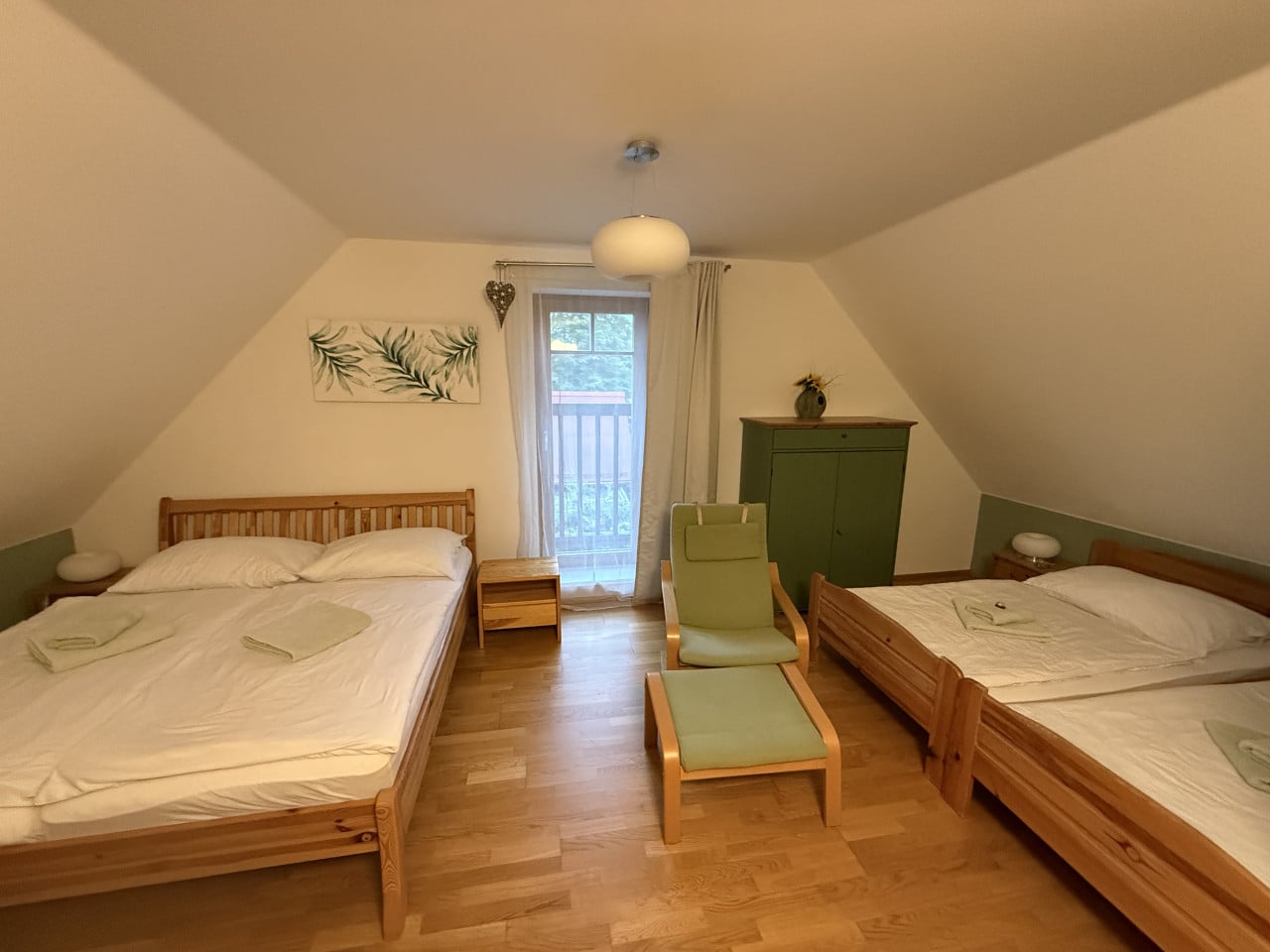 Ložnice se dvěma postelemi, zeleným křeslem a výhledem na balkon.