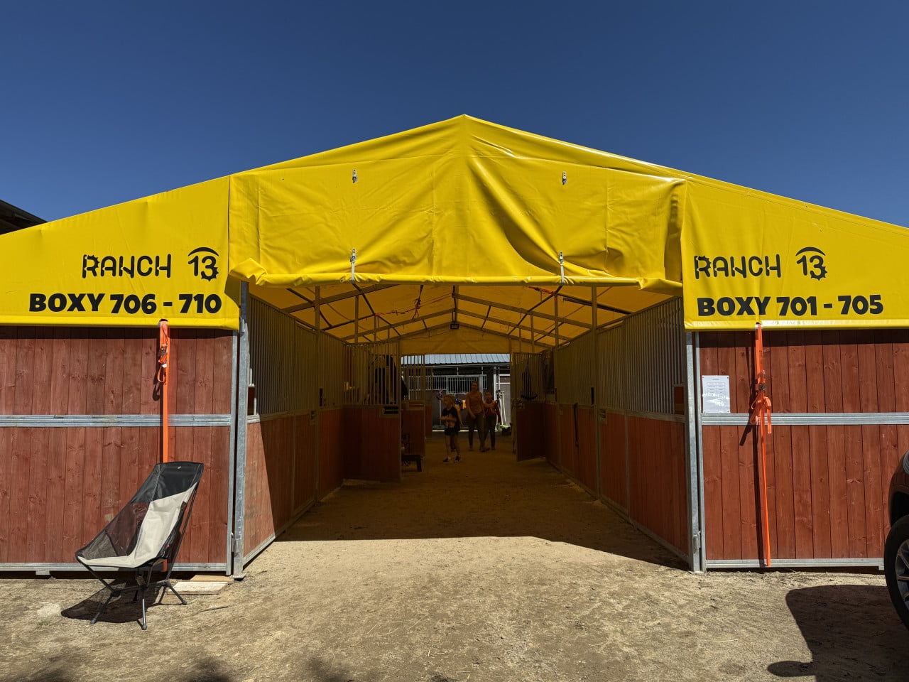 Žlutý stan s boxy pro koně, nápis RANCH 13 a BOXY 701–710.
