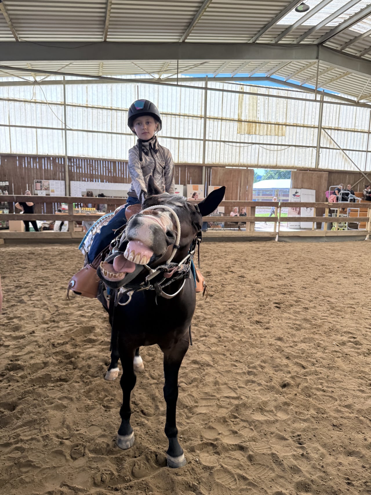 Dítě na pony v hale westernových závodů, kůň s vyceněnými zuby.