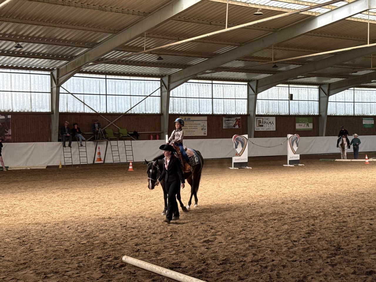 Westernová jezdkyně vede koně v kryté hale Smart Ranch, kolem jsou diváci.