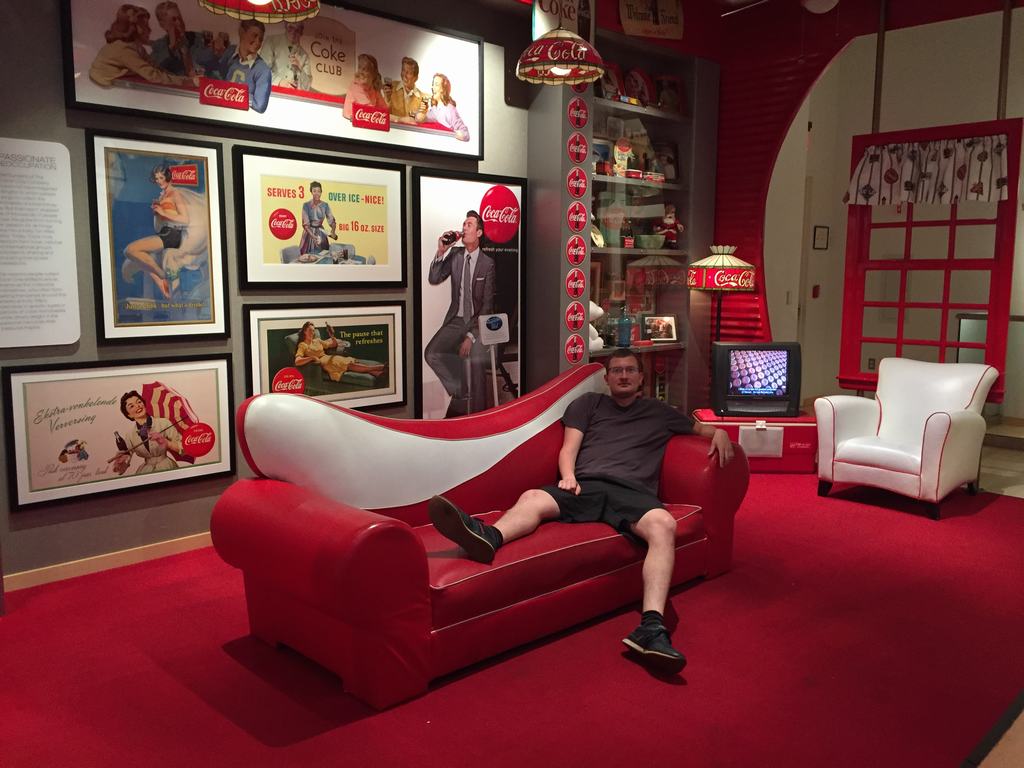 Muž sedí na červené pohovce, kolem vintage plakáty Coca-Cola a Coke.