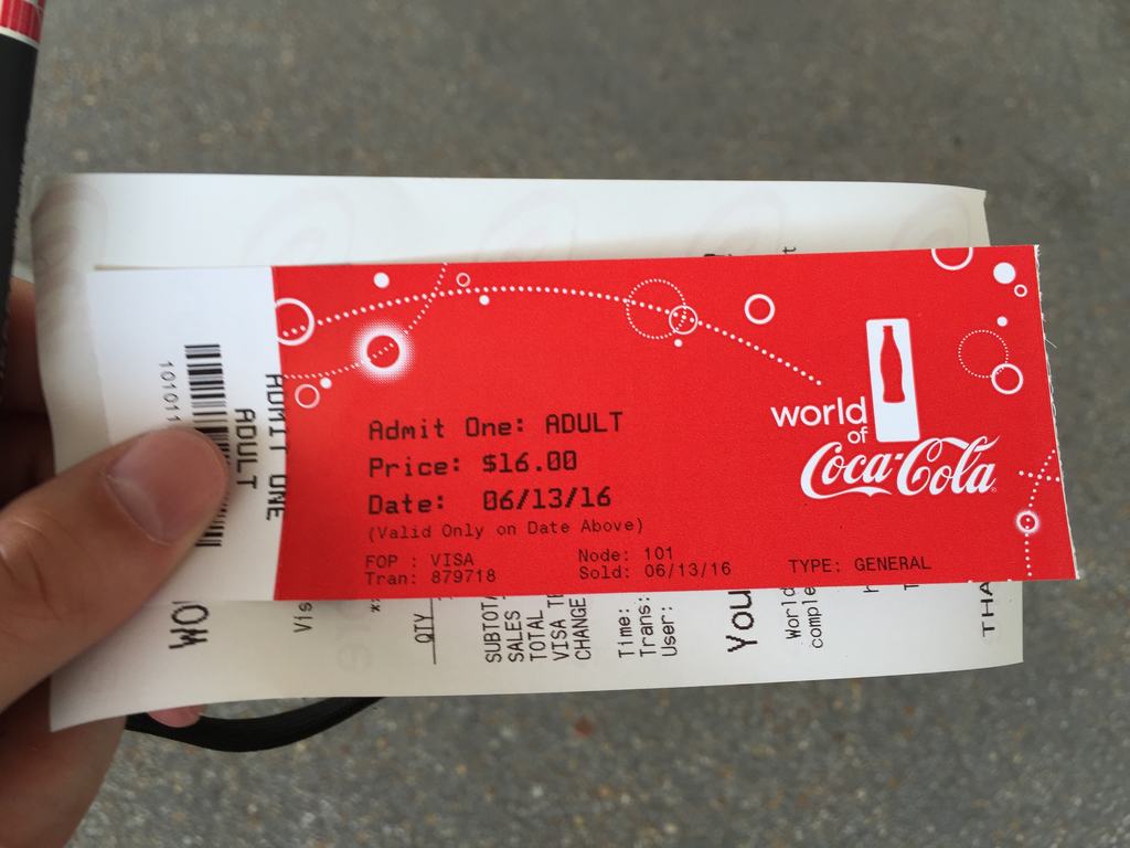 Červená vstupenka World of Coca‑Cola, Admit One ADULT, $16.00, 06/13/16, v ruce.