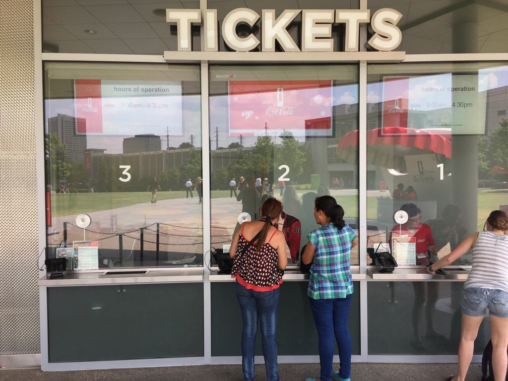 Pokladny s nápisem TICKETS a okénky 1–3, lidé kupují vstupenky.