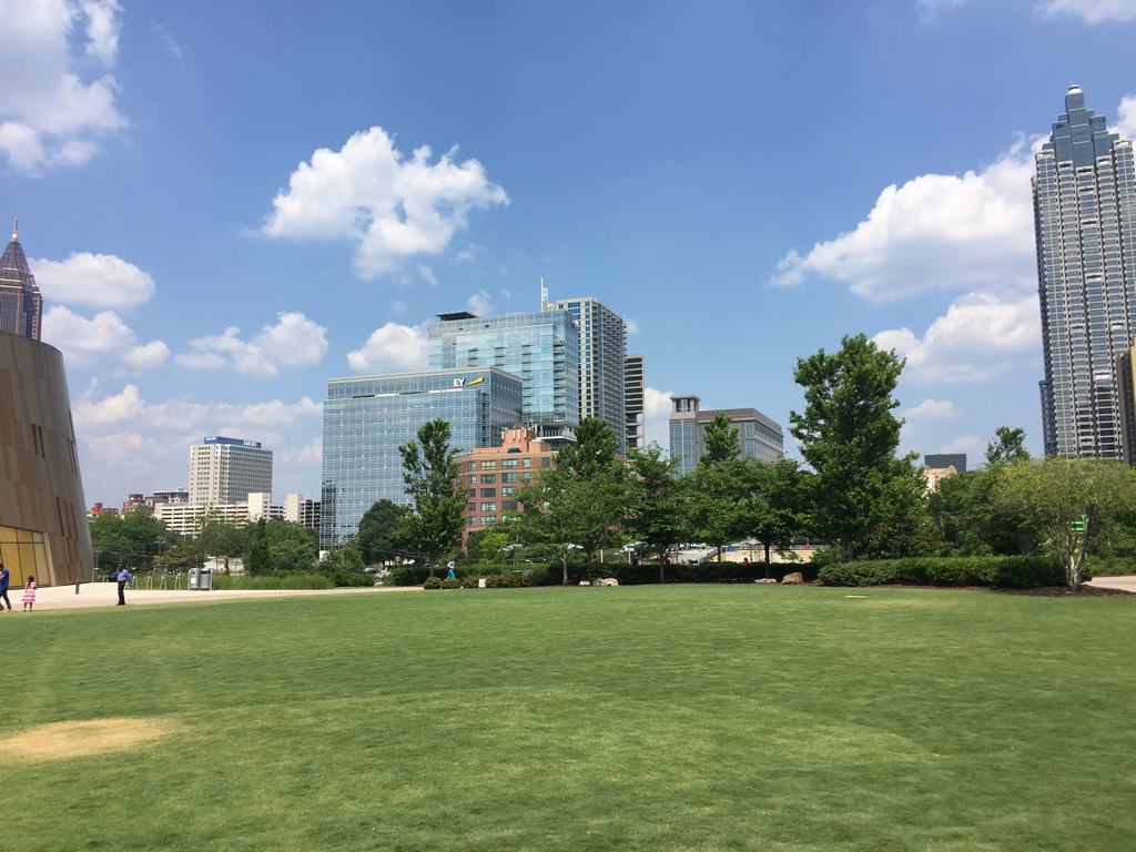 Travnatý park s stromy, panorama mrakodrapů Atlanty a logo EY na budově.