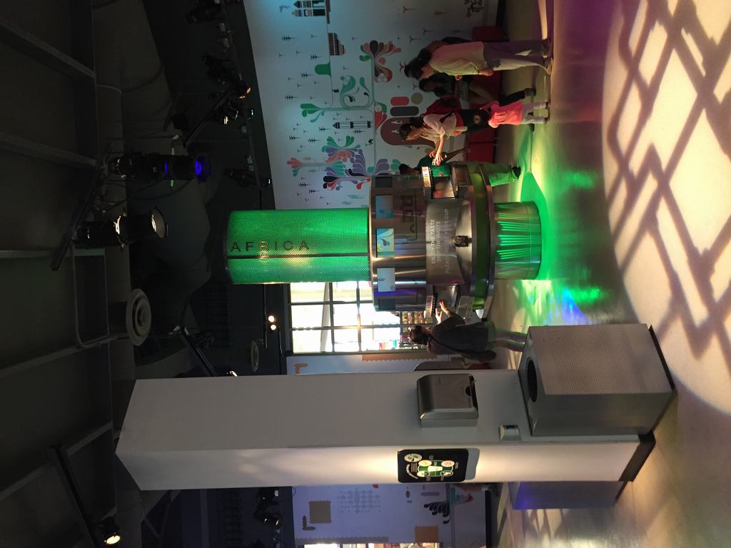 Návštěvníci u ochutnávacího automatu, zelený válec s nápisem AFRICA ve World of Coca‑Cola