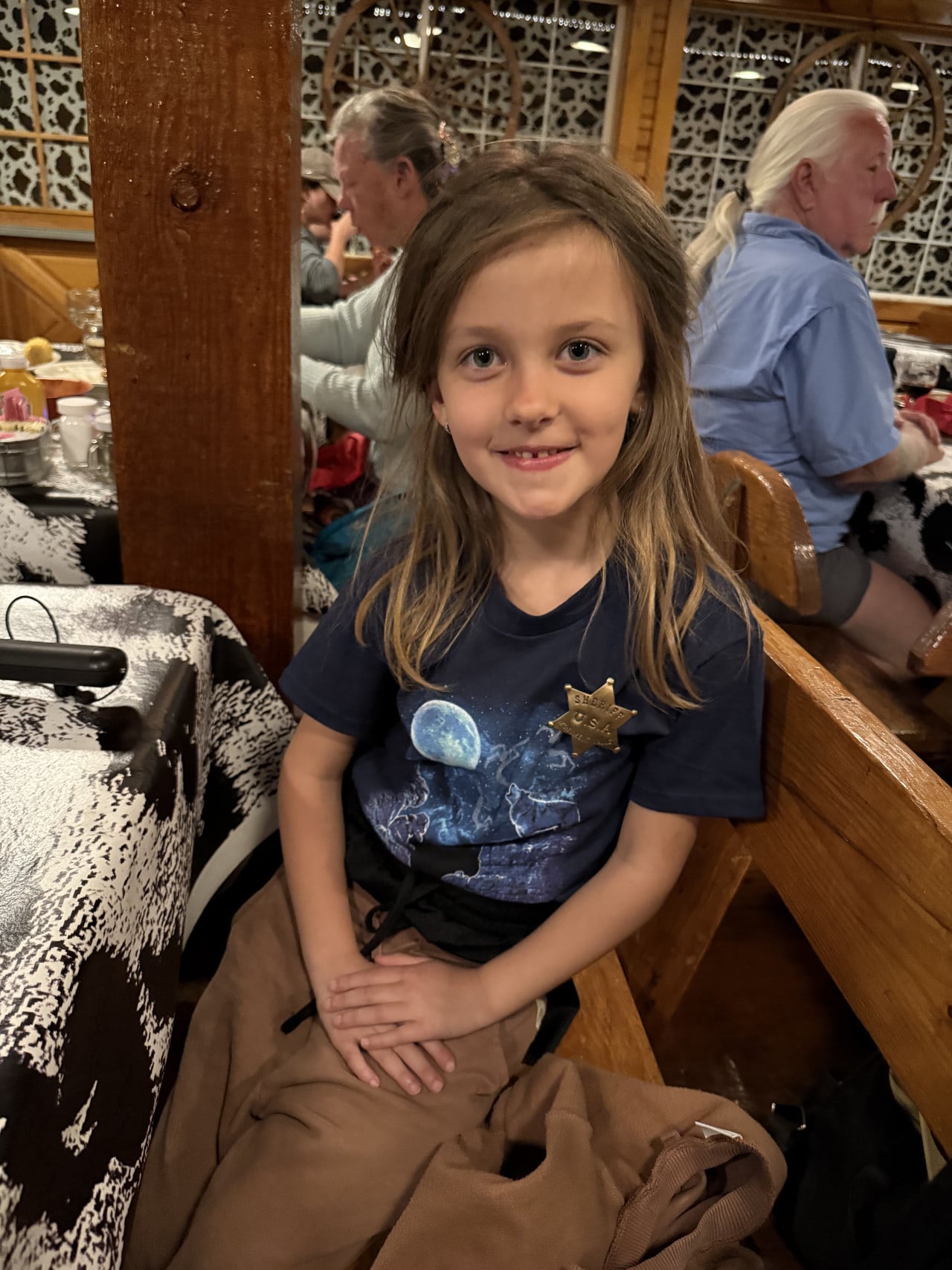 Usmívající se dítě sedí v rustikálním steakhouse s ostatními hosty v pozadí.