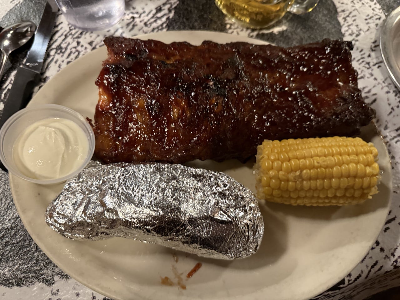 Grilované žebro s pečeným bramborem, kukuřicí a omáčkou na talíři.