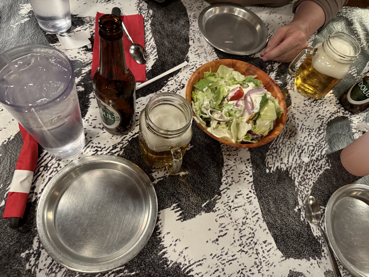 Stůl v steakhouse s pivy, salátem, prázdnými talíři a rukama hostů